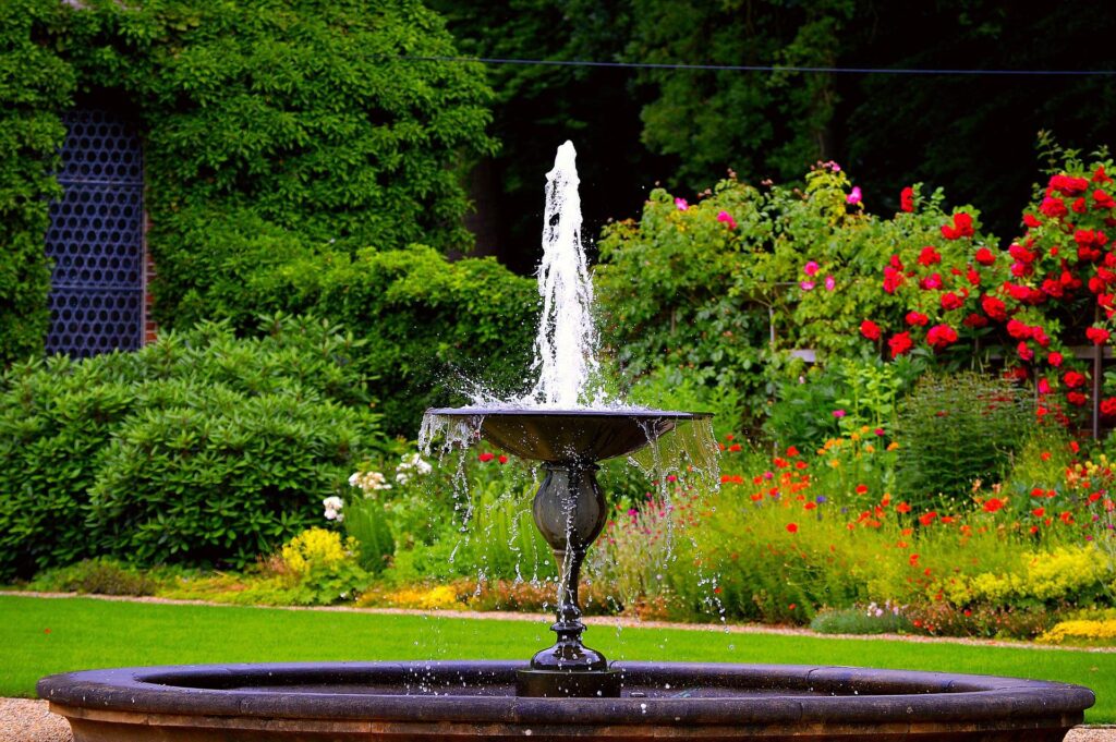 Elegant black pedestal fountain amid colorful roses and greenery