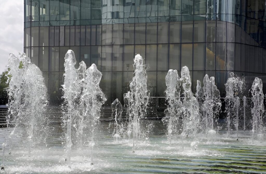 Multiple white water jets erupting before modern glass building