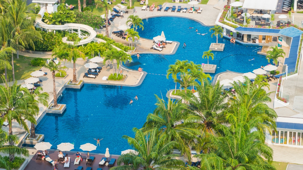 High-angle view of a luxury resort swimming pool featuring custom design curves, integrated water slides, and palm tree landscaping.
